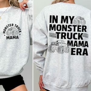 May include: Light gray sweatshirt with black text and graphics. The front features a circular design with a monster truck and the words "Monster Truck Mama." The back displays "In My Monster Truck Mama Era" with monster truck illustrations.