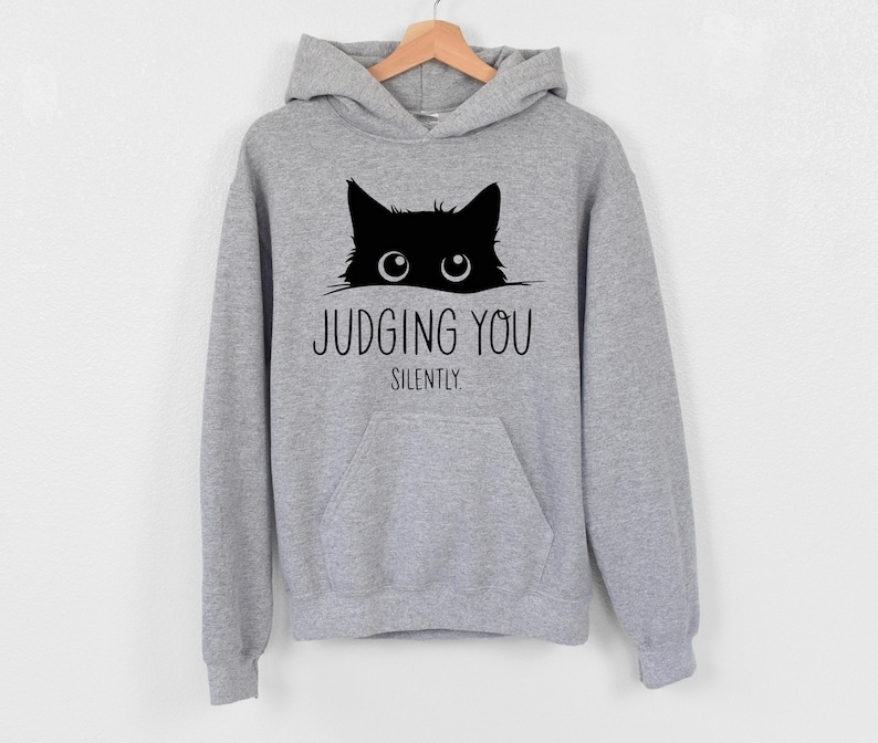 May include: A gray hooded sweatshirt with a black cat peeking out from the top and the text "JUDGING YOU SILENTLY".