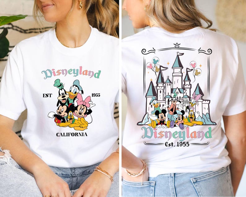 May include: White t-shirt with a colorful Disneyland graphic. The front of the shirt features Mickey Mouse, Minnie Mouse, Goofy, Donald Duck, and Pluto. The back of the shirt features a colorful illustration of Sleeping Beauty's castle with the text "Disneyland Est. 1955".