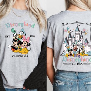 May include: Two gray t-shirts with a Disneyland theme. One shirt features a group of Disney characters including Mickey Mouse, Minnie Mouse, Goofy, Donald Duck, and Pluto. The other shirt features a graphic of the Disneyland castle with the text "Disneyland Est. 1955".