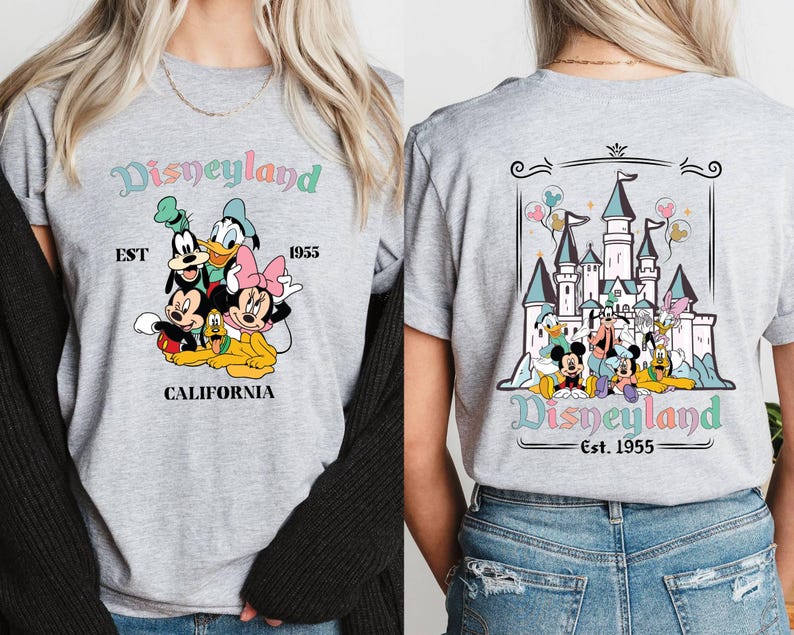 May include: Two gray t-shirts with a Disneyland theme. One shirt features a group of Disney characters including Mickey Mouse, Minnie Mouse, Goofy, Donald Duck, and Pluto. The other shirt features a graphic of the Disneyland castle with the text "Disneyland Est. 1955".