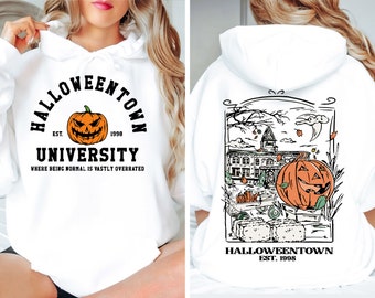 May include: White Halloween-themed hoodie with "Halloweentown University" and a jack-o'-lantern graphic on the front. The back features a detailed illustration of a town scene with a pumpkin and the text "Halloweentown Est. 1998".