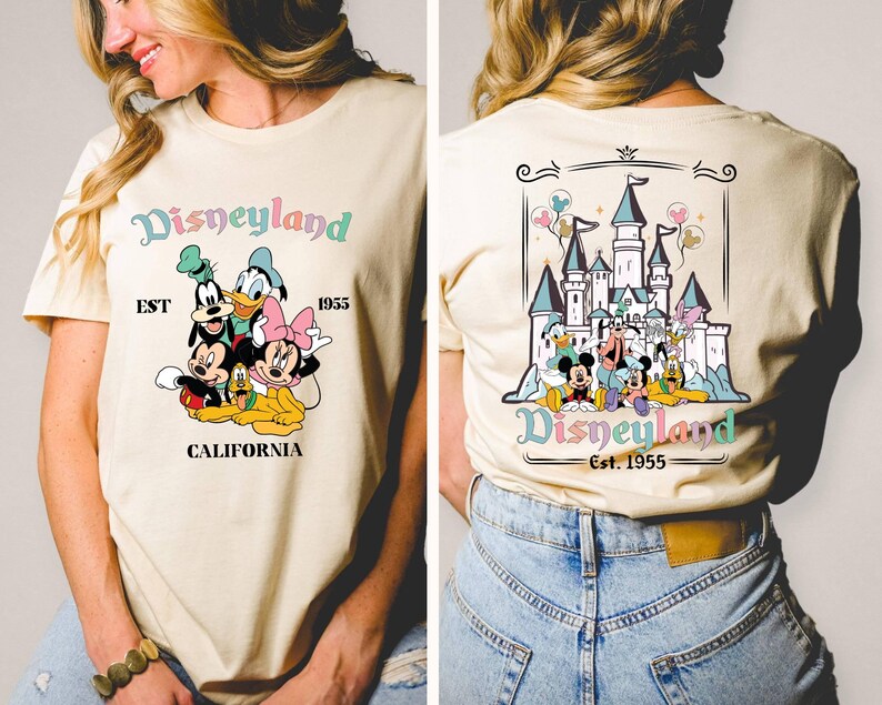 May include: A beige t-shirt with a graphic print of Mickey Mouse and friends in front of the Disneyland castle. The text "Disneyland Est. 1955 California" is printed on the shirt.