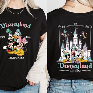May include: Black t-shirt with a colorful Disneyland graphic featuring Mickey Mouse, Minnie Mouse, Donald Duck, Goofy, and Pluto. The graphic includes the text "Disneyland Est. 1955 California". The back of the shirt features a colorful graphic of Sleeping Beauty's castle with the text "Disneyland Est. 1955".