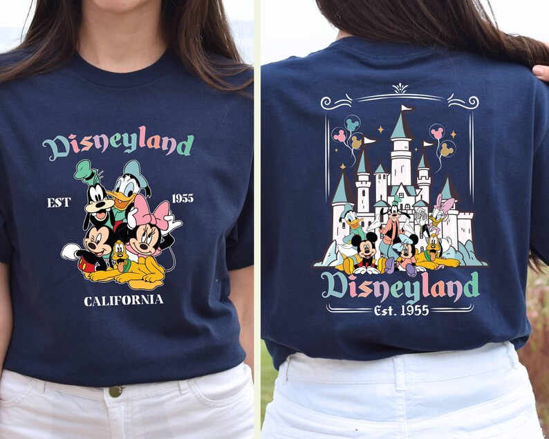 May include: A navy blue t-shirt with a graphic of Mickey Mouse and friends in front of Disneyland. The text "Disneyland Est. 1955 California" is printed on the shirt.