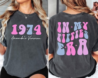 Könnte beinhalten: Ein dunkelgraues T-Shirt mit einer pinkfarbenen und blauen Retro-Grafik, auf der vorne "1974 Amanda's Version" und hinten "In My Fifties Era" steht.