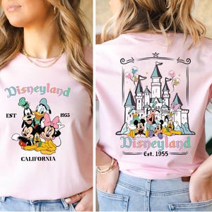 May include: Pink t-shirt with a graphic of Mickey Mouse, Donald Duck, Goofy, Pluto, and Minnie Mouse in front of the Disneyland castle. The text "Disneyland Est. 1955 California" is printed on the shirt.