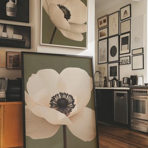 Può includere: Grandi stampe artistiche incorniciate con un primo piano di un fiore di anemone bianco con un centro scuro su uno sfondo verde tenue. L'opera d'arte è esposta in una stanza con altre opere incorniciate e un angolo cottura.
