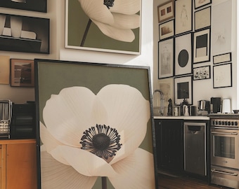 Pode incluir: Grandes impressões de arte emolduradas com um close-up de uma flor de anêmona branca com um centro escuro contra um fundo verde suave. A obra de arte é exibida em uma sala com outras obras emolduradas e uma área de cozinha.