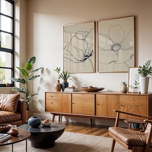 May include: A living room scene featuring a mid-century modern aesthetic. Two large framed floral art prints hang above a wooden sideboard. The room includes leather furniture, plants, and decorative items, creating a warm and inviting atmosphere.