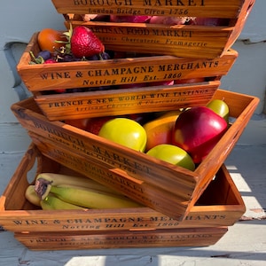 Peut inclure: Quatre caisses en bois empilées les unes sur les autres. Les caisses sont étiquetées avec le texte "Borough Market", "Artisan Food Market", "Wine & Champagne Merchants" et "French & New World Wine Tastings". Les caisses sont remplies de divers fruits et légumes, notamment des bananes, des pommes, des oranges et des mangues.
