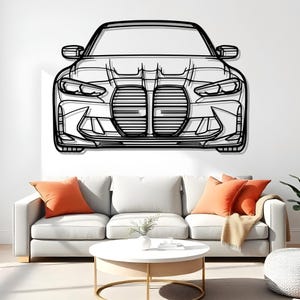 Pode incluir: Arte de parede em metal preto da frente de um carro, com faróis, uma grelha e espelhos laterais. A obra de arte está montada numa parede branca acima de um sofá branco com almofadas laranja e uma mesa de centro redonda.