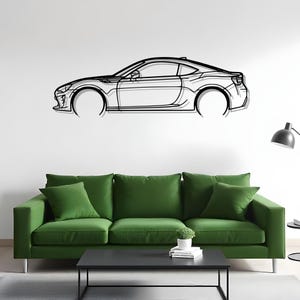 以下が含まれることがあります： 黒い金属製の壁掛けアートで、スポーツカーを描いています。車の側面図で、車輪や窓などの詳細が描かれています。白い壁に設置され、緑のソファと黒いコーヒーテーブルの上にあります。