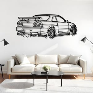 May include: Black metal wall art depicting a sports car. The artwork features a detailed outline of the car's body, including the spoiler, wheels, and exhaust pipes. The car is mounted on a white wall above a white sofa and black coffee table.