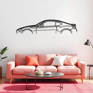 以下が含まれることがあります： 黒い金属製の車の輪郭ウォールアート。 このアートワークは、スポーツカーの側面図を描いています。 車は、オレンジと白のクッションが付いたピンクのソファの上にある白い壁に取り付けられています。 黒いコーヒーテーブルとピンクのラグがソファの前にあります。