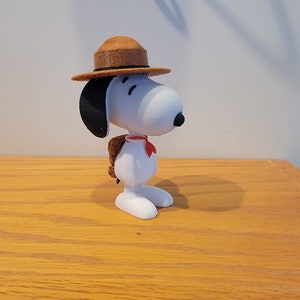 Könnte beinhalten: Eine weiße 3D-gedruckte Figur von Snoopy, der einen braunen Scout-Hut und ein rotes Halstuch trägt.