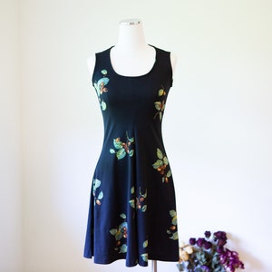May include: A sleeveless black dress with a floral print of green leaves and brown berries. The dress has a scoop neck and a fitted bodice.