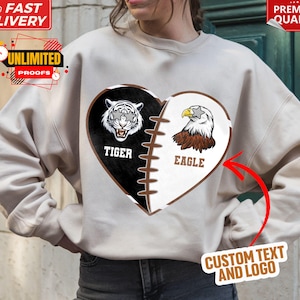 May include: A white sweatshirt with a brown heart design. The heart is split in half, with a tiger on one side and an eagle on the other. The words "Tiger" and "Eagle" are written below each animal. The text "Custom Text and Logo" is written in brown at the bottom of the image.