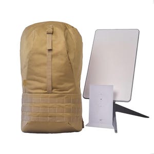 May include: A tan-coloured backpack with a large zipped compartment and a smaller zipped pocket on the front. The backpack has a black strap and a black buckle. The backpack is sitting on a white surface.