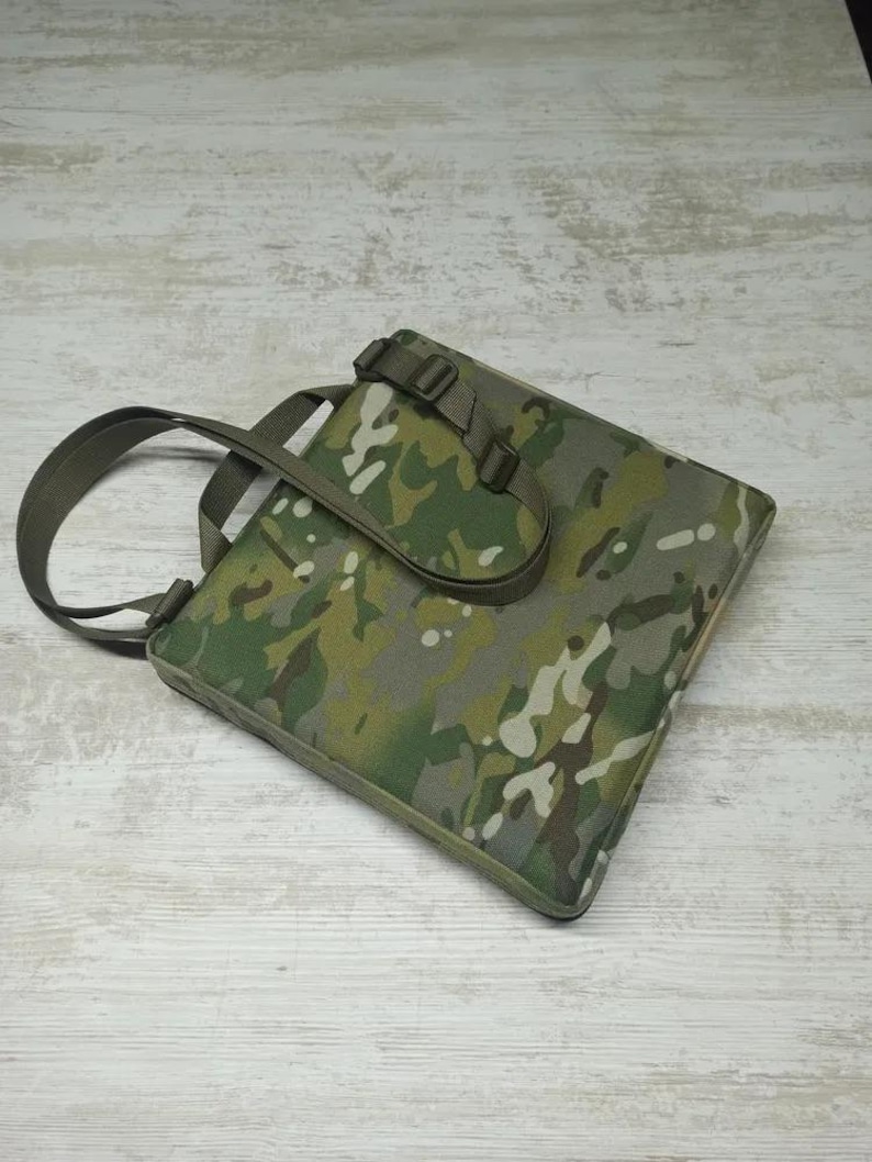 May include: A camouflage-patterned tote bag with a top handle and adjustable shoulder strap. The bag has a flap closure with a buckle.