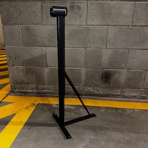 May include: A black metal stand with a triangular base and a vertical post. The stand is designed to hold a sign or other object.
