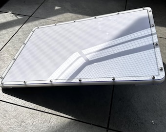 May include: A white rectangular light box with a clear plastic cover and a silver metal frame. The light box is sitting on a tiled floor.
