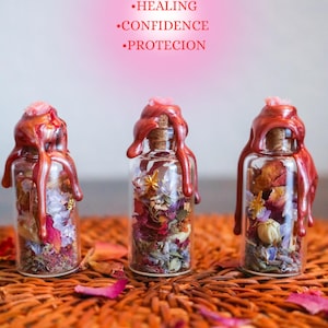 May include: Three clear glass bottles with cork stoppers sealed with red wax. The bottles contain dried flower petals, herbs, and small star-shaped charms. Text above reads: SELF-LOVE, HEALING, CONFIDENCE, PROTECION.