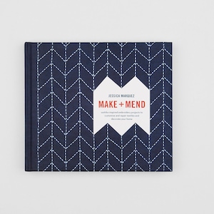 以下が含まれることがあります： ジェシカ・マルケス著「MAKE + MEND」というタイトルの正方形の本。表紙はネイビーブルーで、白いシェブロン模様と白いステッチが施されています。タイトルは、白いひし形のラベルに白と赤のフォントで表示されています。