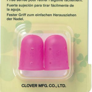Pode incluir: Embalagem com dois dedais de borracha flexíveis rosa, tamanho médio, para costura. A embalagem é verde e branca, com texto em inglês, francês, espanhol e alemão. Os dedais têm 16 mm.