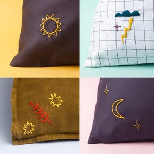 Op de afbeelding: Vier decoratieve kussens met geborduurde weer- en hemelontwerpen. De kussens hebben een zon, een storm met bliksem, sterren en een halve maan. De kussens zijn in verschillende kleuren, waaronder bruin, wit, olijfgroen en donkerpaars.