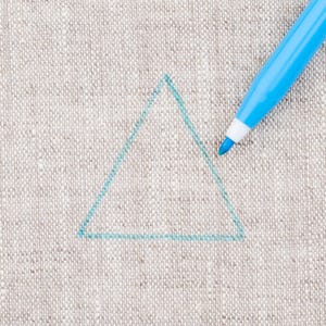 Puede incluir: Un triángulo azul claro dibujado sobre una superficie de tela beige con un bolígrafo marcador azul claro.