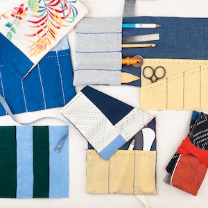 Könnte beinhalten: Sortiment an Stoffnadelbehältern in verschiedenen Farben und Mustern. Die Behälter sind aus Baumwolle und haben unterschiedliche Nähdesigns. Einige Behälter haben Taschen zum Aufbewahren von Nadeln, während andere ein Rolldesign haben.