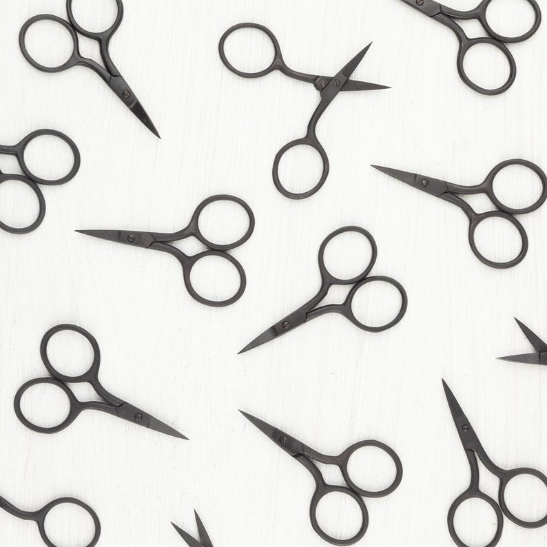 May include: A flat lay of ten black metal small scissors on a white background. The scissors are arranged in a symmetrical pattern.