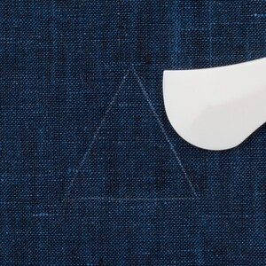 May include: A white plastic tool for tracing a triangle shape on a dark blue fabric.