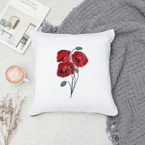 May include: White square throw pillow featuring a red poppy floral design. The pillow has a black trim and a soft, textured appearance. The poppy flowers are detailed with red petals and green stems.