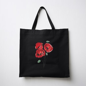 May include: Black tote bag featuring a red poppy flower design. The illustration shows three red poppies with green leaves and thin black stems. The tote bag has black handles and is made of a durable fabric.