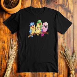 Peut inclure: T-shirt noir avec un motif de quatre perroquets color&eacute;s perch&eacute;s sur une branche. Les perroquets sont vert, bleu, jaune et rose.