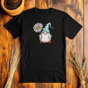 May include: Black t-shirt with a white daisy and a blue gnome holding the flower. The gnome is wearing a blue hat with white polka dots and red shoes.