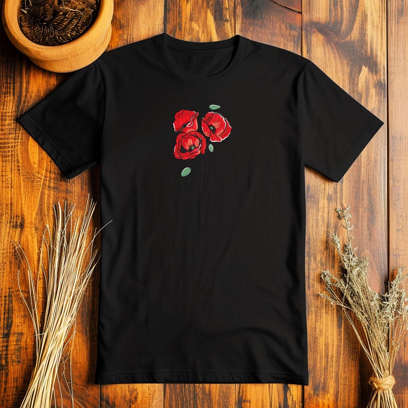 May include: Black t-shirt featuring a floral design of three red poppies with green leaves. The poppies are stylized with detailed petals and a simple stem. The shirt is made of a soft material.