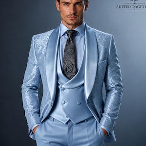 May include: A light blue suit featuring a patterned blazer with a shawl lapel, a matching double-breasted vest, and a dark grey paisley tie. The ensemble includes a light blue dress shirt and trousers, with the Suited Together logo visible.