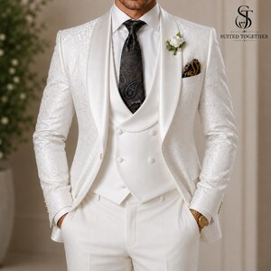 May include: A white three-piece suit featuring a patterned blazer with a shawl lapel, a double-breasted vest, and matching trousers. A black paisley tie is worn with a white shirt, and a white flower boutonniere is pinned to the lapel.