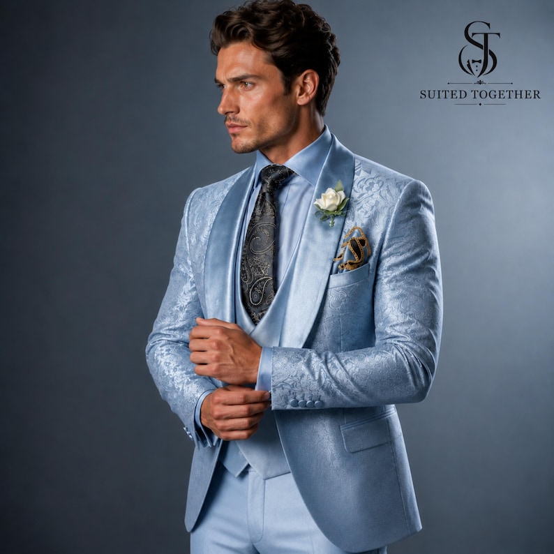 May include: A light blue blazer and matching vest featuring a tonal floral jacquard pattern, paired with a light blue dress shirt, a dark grey paisley tie, and a white floral boutonniere. The Suited Together logo is visible in the top right corner.