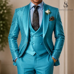 May include: A bright turquoise suit featuring a patterned blazer with a shawl lapel, a double-breasted waistcoat, and matching trousers. The ensemble includes a light blue dress shirt, a dark patterned necktie, and a white floral lapel pin.