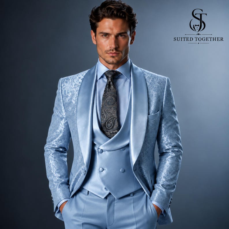 May include: A light blue suit featuring a patterned blazer with a shawl lapel, a matching double-breasted vest, and a dark grey paisley tie. The ensemble includes a light blue dress shirt and trousers, with the Suited Together logo visible.