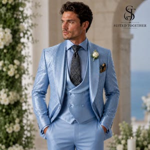 May include: A light blue suit featuring a patterned blazer, a double-breasted waistcoat, and matching trousers. The ensemble includes a light blue dress shirt, a dark grey paisley tie, and a white floral boutonniere on the lapel.