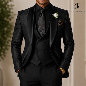 May include: A black three-piece suit featuring a patterned blazer with a satin shawl lapel, a solid black double-breasted vest, and a black paisley tie. A white floral boutonniere is pinned to the lapel. The logo SUITED TOGETHER is visible.