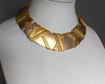 May include: A gold-toned statement necklace with a geometric design. The necklace is made of interlocking pieces that create a bold and modern look.