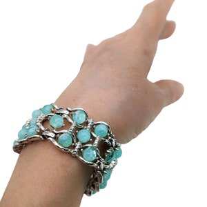 May include: A silver bracelet with light blue beads. The bracelet is made of a chain with a woven design. The beads are round and have a smooth finish.