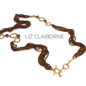 May include: A multi-strand beaded necklace in brown with gold accents and a toggle clasp. The necklace is knotted and features the Liz Claiborne brand name.