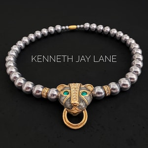 Peut inclure: Un collier Kenneth Jay Lane composé d'un rang de perles gris métallisé et d'un pendentif central en forme de tête de panthère dorée. La panthère a des yeux en pierre verte, des cristaux clairs sur le front et un anneau doré suspendu.